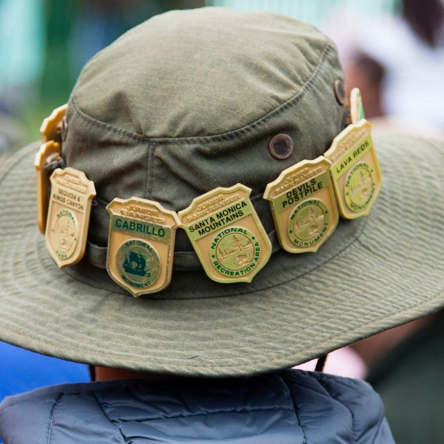 Person in bucket hat, brim lined with golden junior ranger badges.