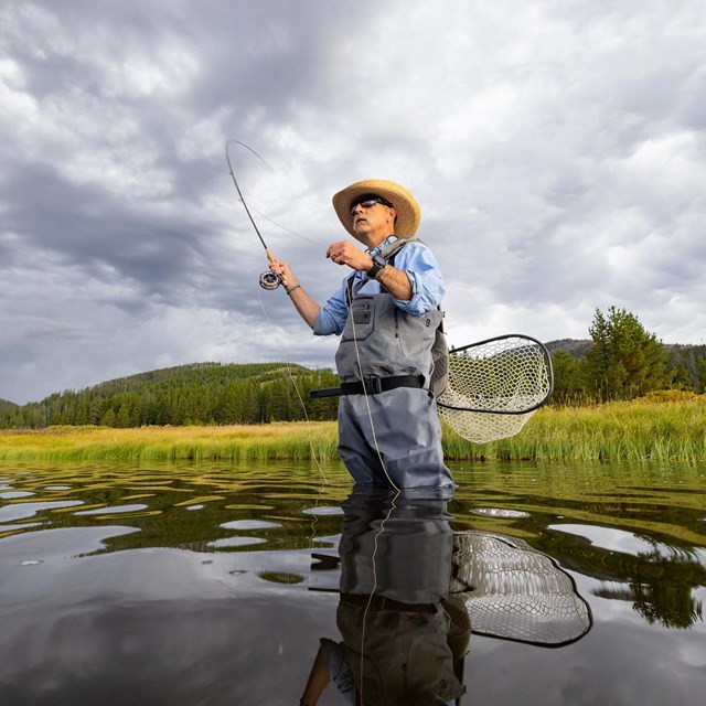 Angler fishing in a lake with a mountain in the background.