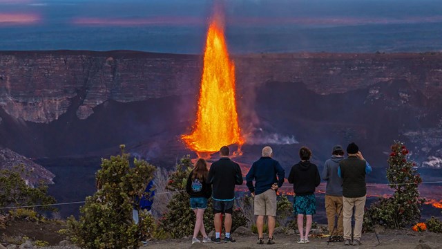 A group of people at an overlook viewing a high fountain of lava. 